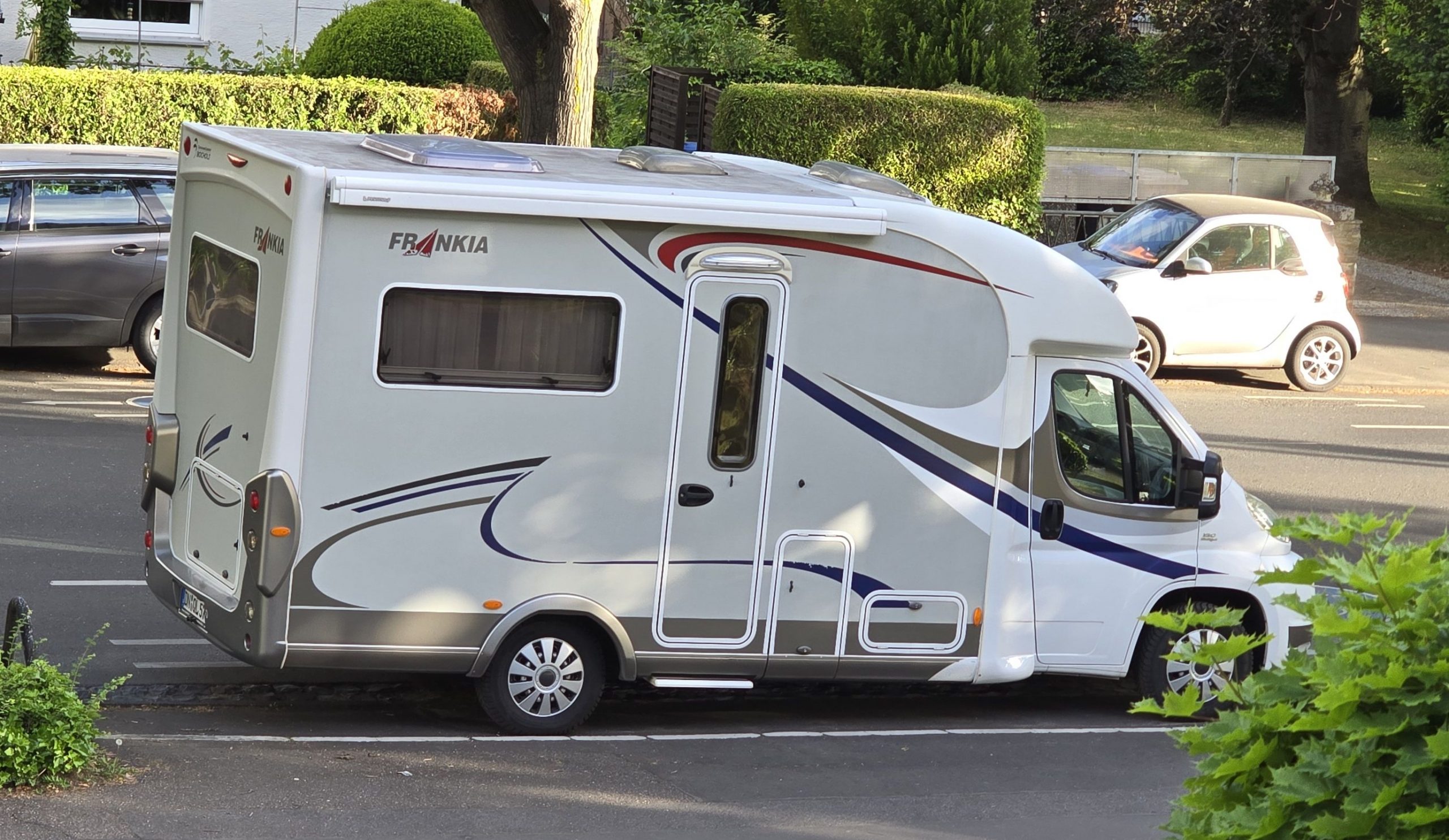 Wohnmobil parkt neben der Straße, vom 1. Stock aus gesehen, im Hintergrund parkende Fahrzeuge und grüne Vorgärten